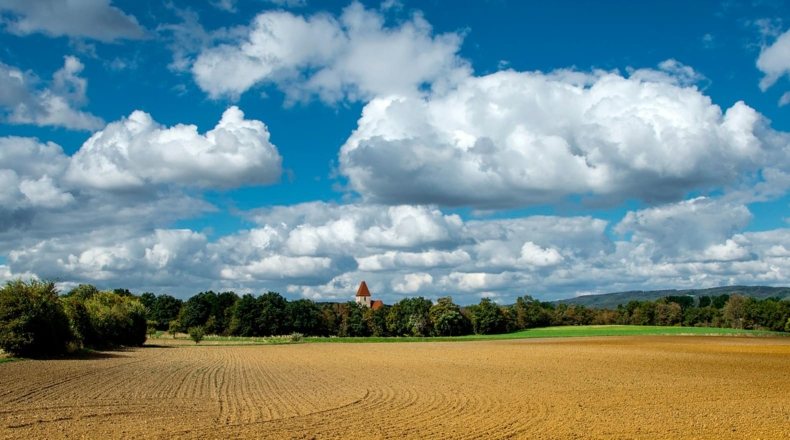 Imagen de un amplio paisaje que cuenta con un amplio territorio urbanizable, con una construcción al fondo, tras una zona de árboles
