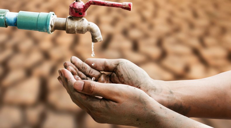 Manos abiertas bajo un grifo seco, simbolizando la escasez de agua en España, con un paisaje de sequía visible al fondo, destacando la urgencia de la crisis climática